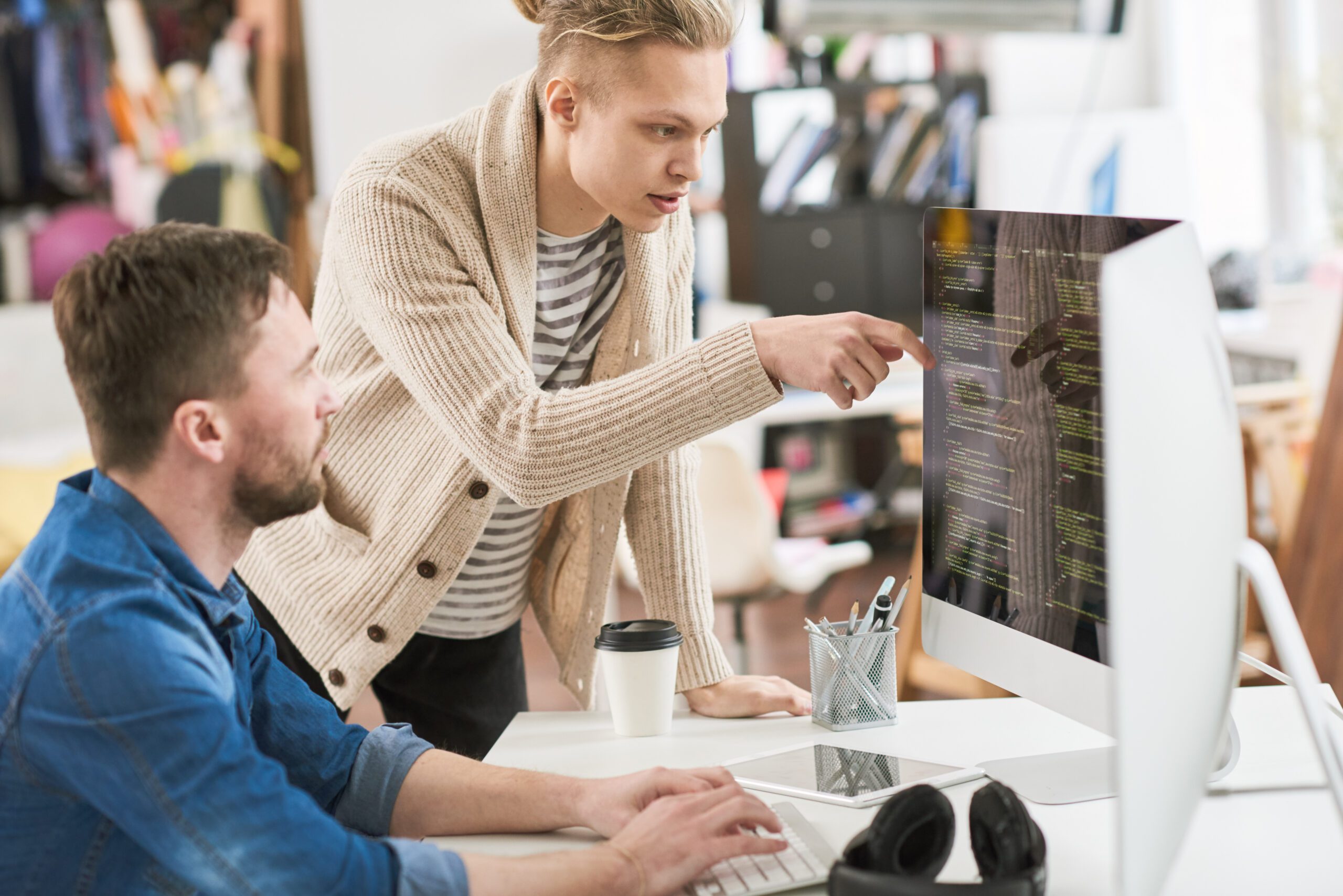 Portrait of two creative young people writing code at desk and  using computer while collaborating with colleague on startup project in modern office