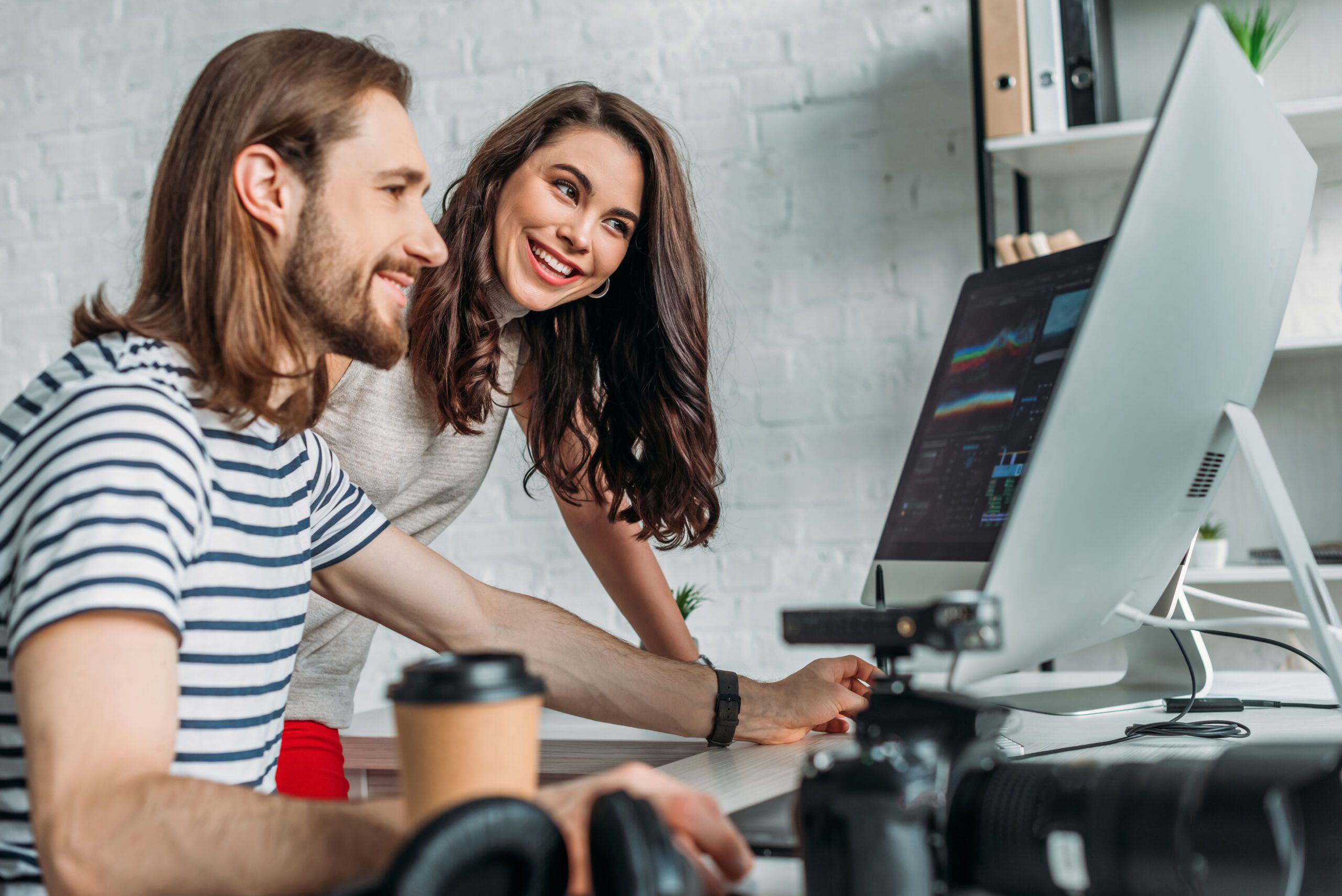 selective focus of happy art editor looking at computer monitor near coworker